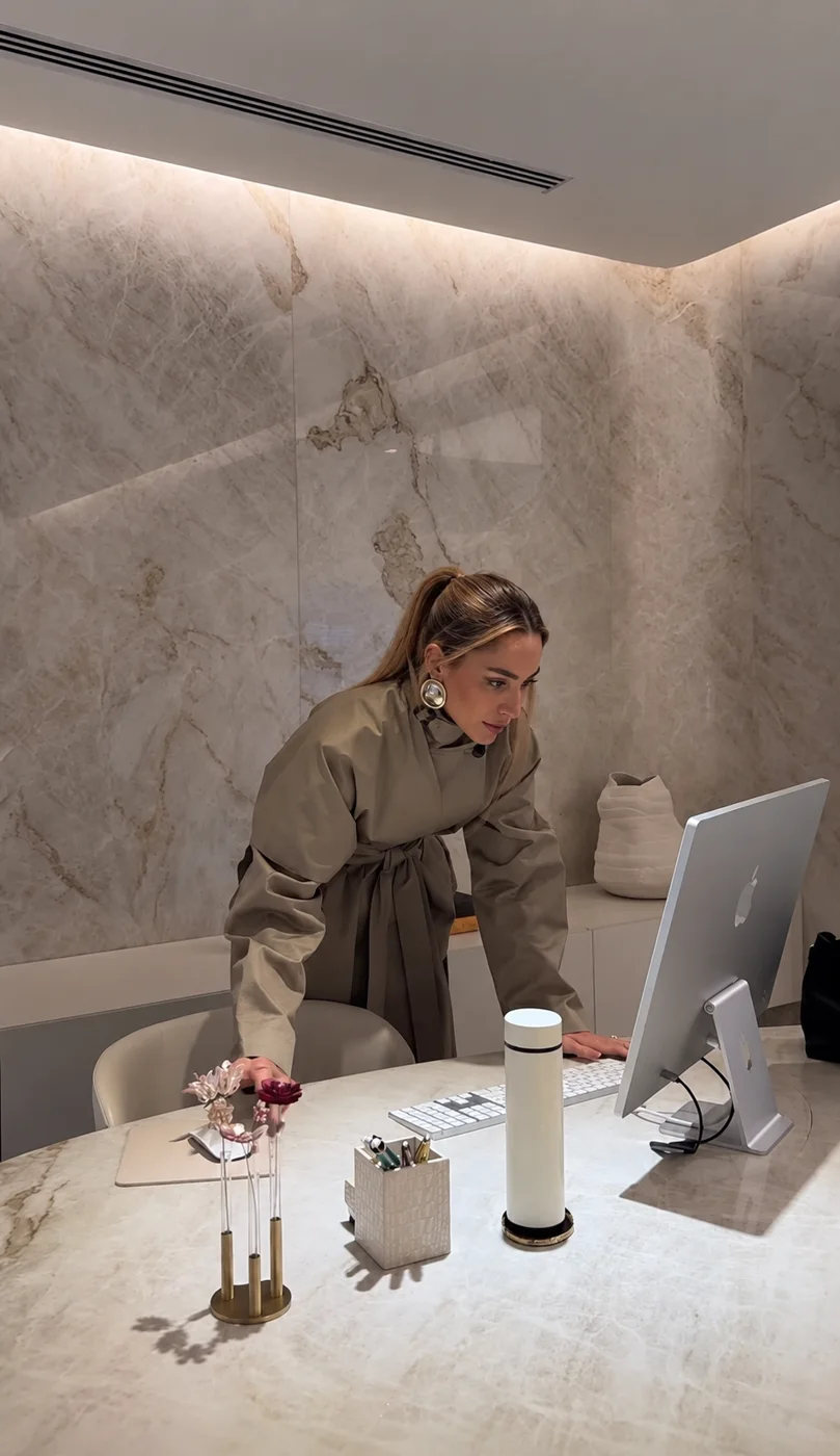 Aleksandra leaning over a marble desk, working at a desktop computer in a neutral office