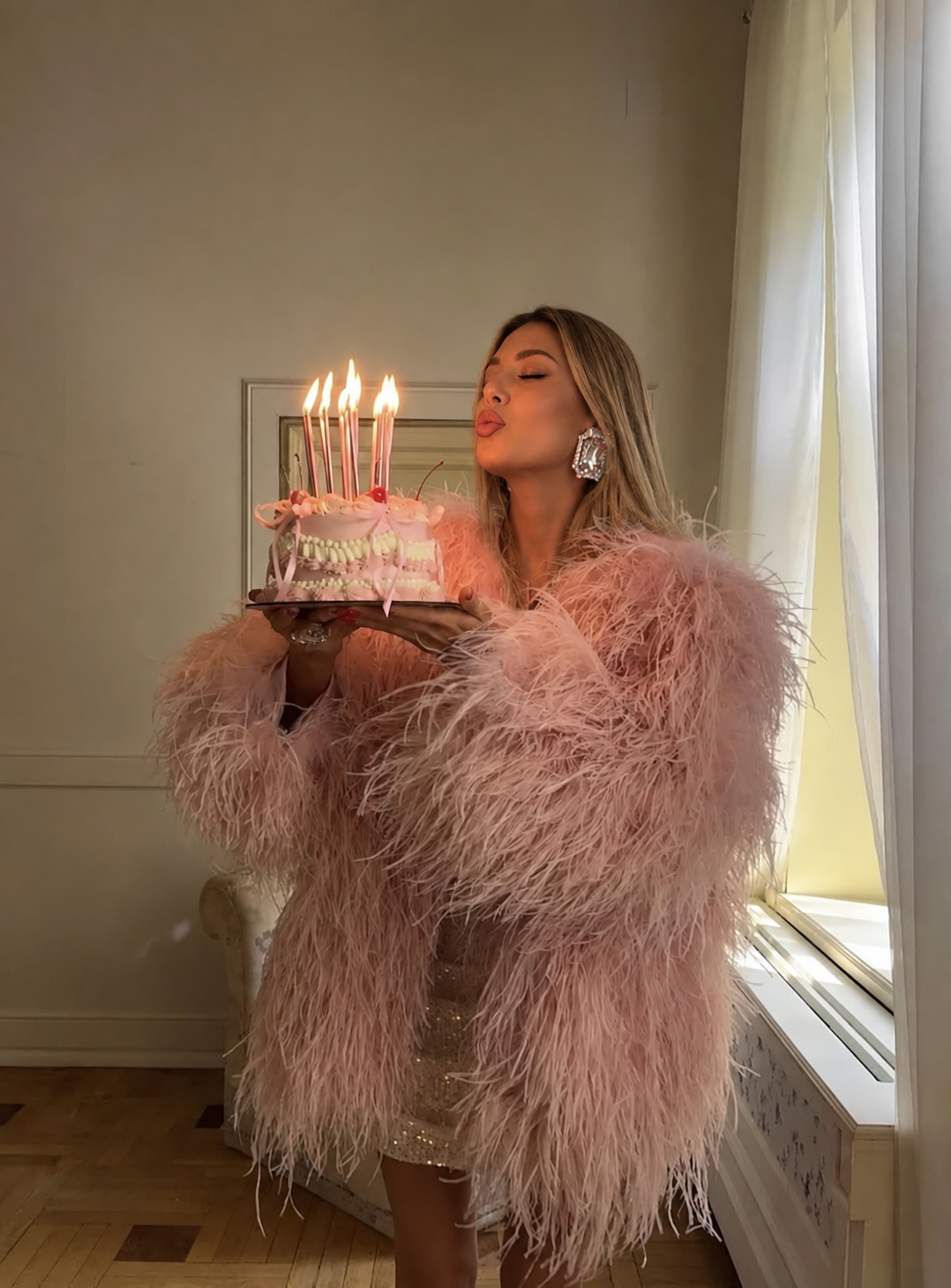 Celebrating in a pink feather coat with a birthday cake