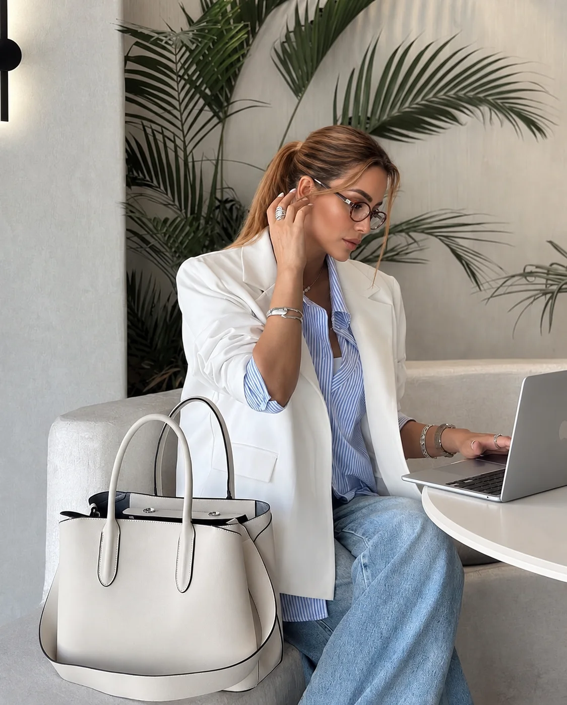 Aleksandra in a white blazer and glasses, working on a laptop at a café table
